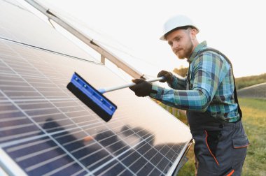 Sert bir şapka ve eldiven takan işçiler kirli güneş panellerini bir cam sileceğiyle temizliyor ve yenilenebilir enerji verimliliğini sağlıyor.