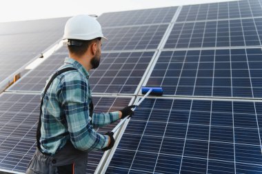 Sert bir şapka ve eldiven takan işçiler güneş panelini temizliyor, verimli yeşil enerji üretimi için gerekli bakımı yapıyorlar.