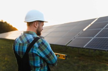 Teknisyen sabit şapka takıyor ve bir seviyeyi tutuyor, çiftliğe güneş panelleri kuruyor, temiz enerji üretiyor.