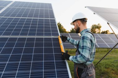 Sert şapka takan ve koruyucu eldiven takan genç bir adam güneş panelini ayarlamak için bir seviye kullanıyor ve enerji üretimi için doğru açıyı sağlıyor.
