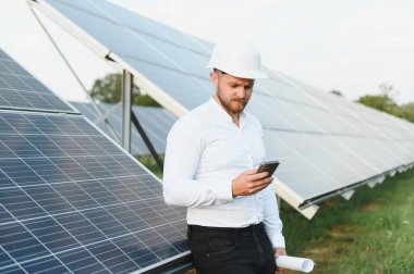 Yenilenebilir enerji çiftliğindeki güneş panellerini izleyen bir mühendis veri analizi için akıllı telefon kullanıyor.