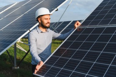 Sakallı erkek mühendis güneş paneli takıyor, güneş enerjisi çiftliğinde çalışıyor. Yeşil teknolojiyi ve sürdürülebilirliği teşvik etmek
