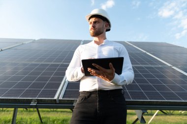 Elinde bir tablet tutan mühendis, güneş panellerini denetliyor ve sürdürülebilir bir enerji istasyonunda temiz enerji üretimini izliyor.