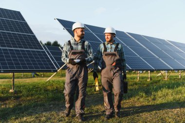 İki mühendis, sürdürülebilir yenilenebilir enerjiyi yönetmek için büyük bir güneş enerjisi santralinde yürürken iş konuşuyorlar.