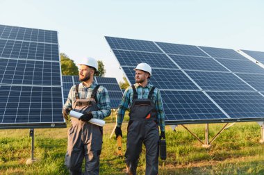 Fotovoltaik modülleri inceleyen, etkin güneş enerjisi üretimi ve sürdürülebilirliği sağlayan iki işçi.