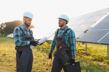 Güneş paneli alanında proje planını tartışan iki mühendis yeşil enerji gelişimine odaklanıyor.
