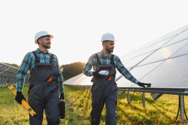 Güneş panellerini yürüten ve kontrol eden, sürdürülebilir enerji üretimini sağlayan baret ve tulum giyen iki işçi