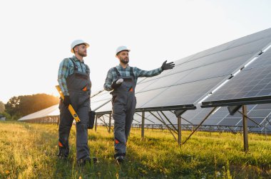 İki mühendis, bir fotovoltaik enerji istasyonunda güneş panellerini inceleyerek yeşil enerjiye odaklanıyorlar.