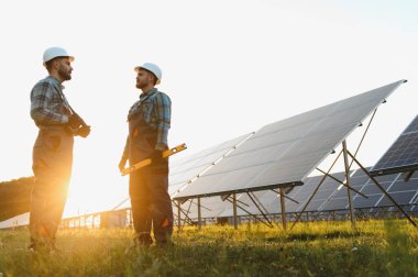 Günbatımında güneş panellerini kontrol ederken projeyi tartışan iki mühendis, temiz yenilenebilir enerji üretiyor