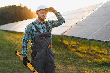 Sert şapkalı teknisyen ve güneş paneli kuran yeşil enerjili güneş paneli gün batımında temiz elektrik üreten