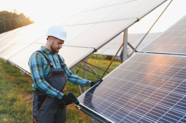 Bir elektrik santraline güvenlik ekipmanı takan ve güneş panelleri kuran erkek işçi temiz elektrik üretiyor.