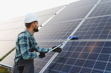 Erkek teknisyen sıkı bir şapka takıyor ve güneş panellerini temizliyor. Sürdürülebilir enerji bakımı ve yeşil işler kavramı