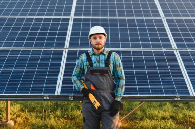 Büyük güneş panellerinin önünde duran teknisyen işçisi yenilenebilir enerji altyapısı kuruyor.