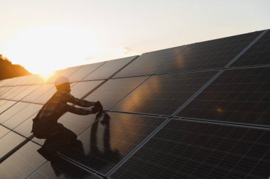 Günbatımında güneş paneli üzerinde çalışan teknisyen, yenilenebilir enerji ve yeşil endüstriyi destekliyor.