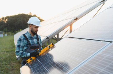 Erkek işçi sabit şapka takıyor ve güneş panelleri kuruyor. Uygun hizalama için ruh seviyesi kullanıyor.
