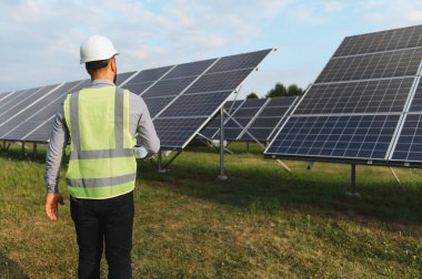 Güneş enerjisi santralinde duran çelik yelek giyen mühendis sürdürülebilir enerji üretimi üzerinde çalışıyor.