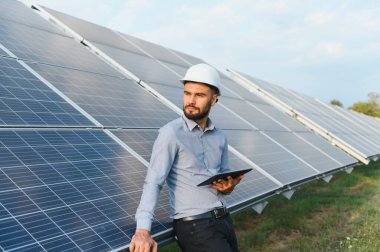 Sert şapkalı mühendis, büyük güneş panellerini tabletle denetliyor, yenilenebilir enerji teknolojisi ve sürdürülebilir güç üzerine odaklanıyor.