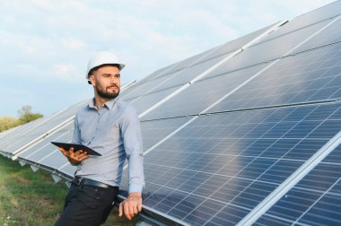 Tabletli sert şapka takan adam güneş enerjisi kurulumuna bakıyor. Yenilenebilir elektrik üretim sistemi