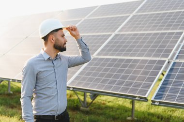 Başlık takan mühendis, sürdürülebilir teknoloji ve yeşil enerjiyi temsil eden bir alandaki güneş panellerinin verimliliğini kontrol ediyor.