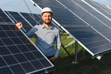 Sert bir şapka takan genç adam, bir güneş enerjisi santralinde güvenle duruyor, temiz yenilenebilir enerjiyi teşvik ediyor.