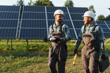 Mühendisler, yenilenebilir enerji santraline güneş panelleri kurarken iş kıyafetleri giyip planlarını tartışıyorlar.