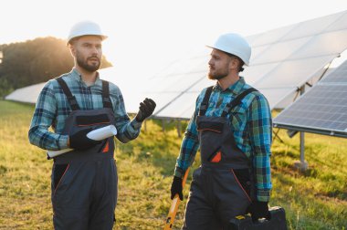 Sert şapka takan iki mühendis yenilenebilir enerji santralinde güneş enerjisi kurulumu planlarını tartışıyorlar.