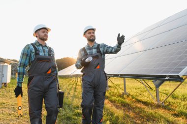 İki mühendis bir alanda güneş panellerini inceleyerek yenilenebilir enerji projesini tartışıyorlar.
