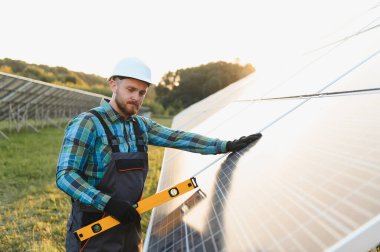 Sert başlıklı işçiler güneş panelinin hizasını yeşil enerji üretiminde kalite ve sürdürülebilirliği güvence altına alarak bir seviye ile kontrol ediyorlar