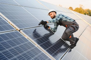 Yeni güneş panelleri kurmak için elektrikli matkap kullanan işçiler, fotovoltaik elektrik santralinde yenilenebilir enerji geliştiriyorlar.