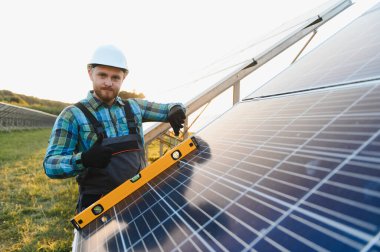 Güneş paneli kuran erkek teknisyen, bir güneş çiftliğinde verimli bir yenilenebilir enerji üretimi sağlamak için, bir seviye aracı ile hizalama kontrol