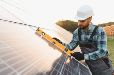 Bir alana güneş panelleri kuran mühendis, yeşil enerji ve sürdürülebilirliği destekleyen bir seviye aracı ile hizalama kontrol
