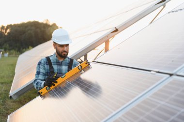 Mühendis, bir elektrik santralinde verimli bir yeşil enerji üretimi sağlamak için güneş panelinin hizalanmasını bir seviye aracıyla kontrol ediyor