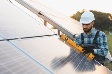 Başlık ve tulum takan mühendis kurulum sırasında ruh seviyesini kullanarak güneş panelinin seviyesini kontrol ediyor.