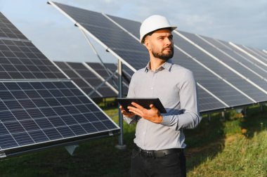 Mühendis, elinde tablet tutarak güneş panellerini kontrol ediyor. Yenilenebilir enerji geleceği, yeşil teknoloji kavramı