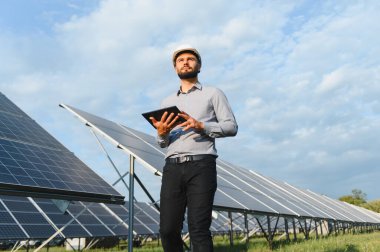 Sert şapka takan mühendis güneş fotovoltaik panel performansını kontrol ederek güneş çiftliğinde sürdürülebilir yeşil enerjinin verimliliğini sağlıyor.