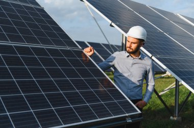 Sert kaskta sakallı mühendis güneş pili alanını kontrol ediyor, sürdürülebilir enerji üretimini ve yeşil teknoloji operasyonunu güvence altına alıyor