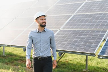 Kemerli şapka takan ve gözünü kaçıran adam, temiz ve sürdürülebilir enerji sağlayan güneş panellerini inceliyor.
