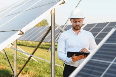Bir güneş enerjisi santralinde dijital tablet kullanarak yeşil yenilenebilir enerji verimliliği sağlayan sabit kasklı mühendis.