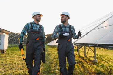 İki mühendis güneş paneli alanında enerji üretimini tartışıyorlar, verimli ve sürdürülebilir enerji üretimini sağlıyorlar.