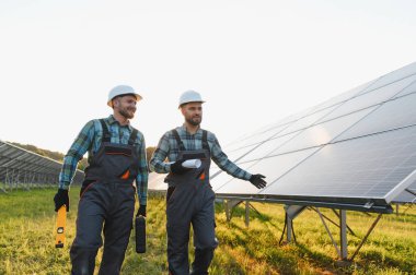 Güneş batımında güneş paneli alanında yürüyen ve yeşil enerji projesini tartışan iki mühendis.