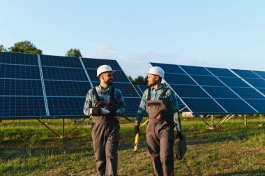 İki mühendis, sürdürülebilir yeşil enerji üretimini yöneten, büyük bir güneş enerjisi santralinde yürürken iş konuşuyorlar.
