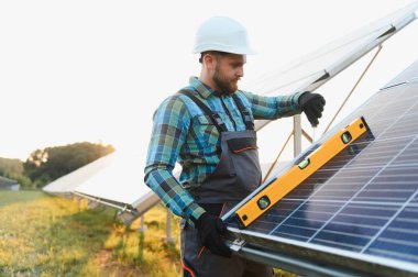 Güvenlik kaskı ve tulumlu işçiler güneş panelinin ruh seviyesini kontrol ederek verimli bir yenilenebilir enerji üretimi sağlıyorlar.