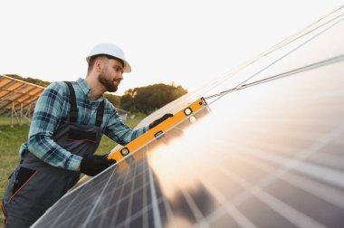 Genç teknisyen güneş panelinin hizalanmasını dikkatlice kuruyor ve kontrol ediyor, güneş enerjisi alanında verimli ve sürdürülebilir enerji üretimini sağlıyor