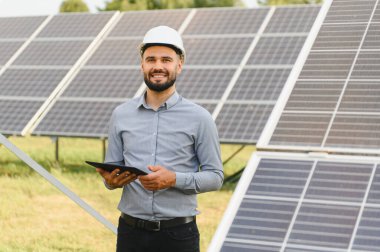 Sakallı mühendis elinde dijital tablet tutarak güneş paneli kurulumunu kontrol ederek sürdürülebilir temiz enerji üretimini sağlıyor.