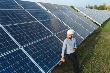 Güneş fotovoltaik panellerini denetleyen, yenilenebilir enerji ve sürdürülebilir teknolojiyi temsil eden bir adam.