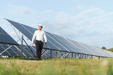 Gündüz yenilenebilir enerji sahasında büyük güneş panellerini inceleyen genç mühendis fotovoltaik kurulum ve bakımı değerlendiriyor.