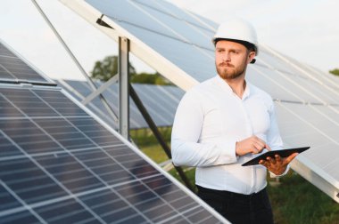 Güneş enerjisi santralinde çalışan bir mühendis, enerji sistemlerini dijital tabletle kontrol ediyor.