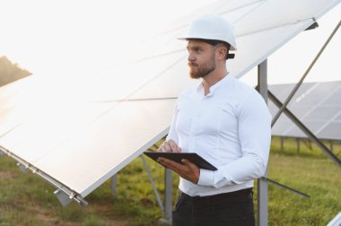 Başlık takan mühendis güneş enerjisi tarlasında tablet kullanıyor. Yenilenebilir enerji ve sürdürülebilir teknoloji kavramı