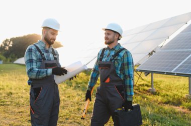 Bir güneş enerjisi santralinin planlarını inceleyen, yenilenebilir enerji teknolojisini yöneten iki işçi.