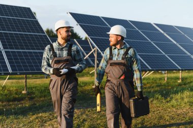 Bir güneş enerjisi santralinde güvenlik kaskı ve tulumu takan mühendisler, sürdürülebilir enerji geçişi için çalışıyorlar.